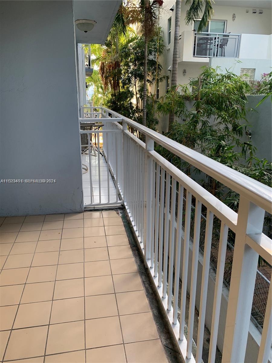 A tiled balcony features a white metal railing and overlooks lush green trees — 947 Lenox Ave # 204, Miami Beach FL 33139, MIAMI BEACH, FL