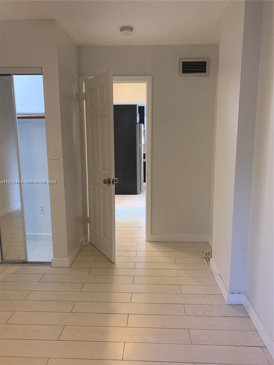 A room with light-colored wood-look flooring leads through an open door into a kitchen area — 947 Lenox Ave # 204, Miami Beach FL 33139, MIAMI BEACH, FL