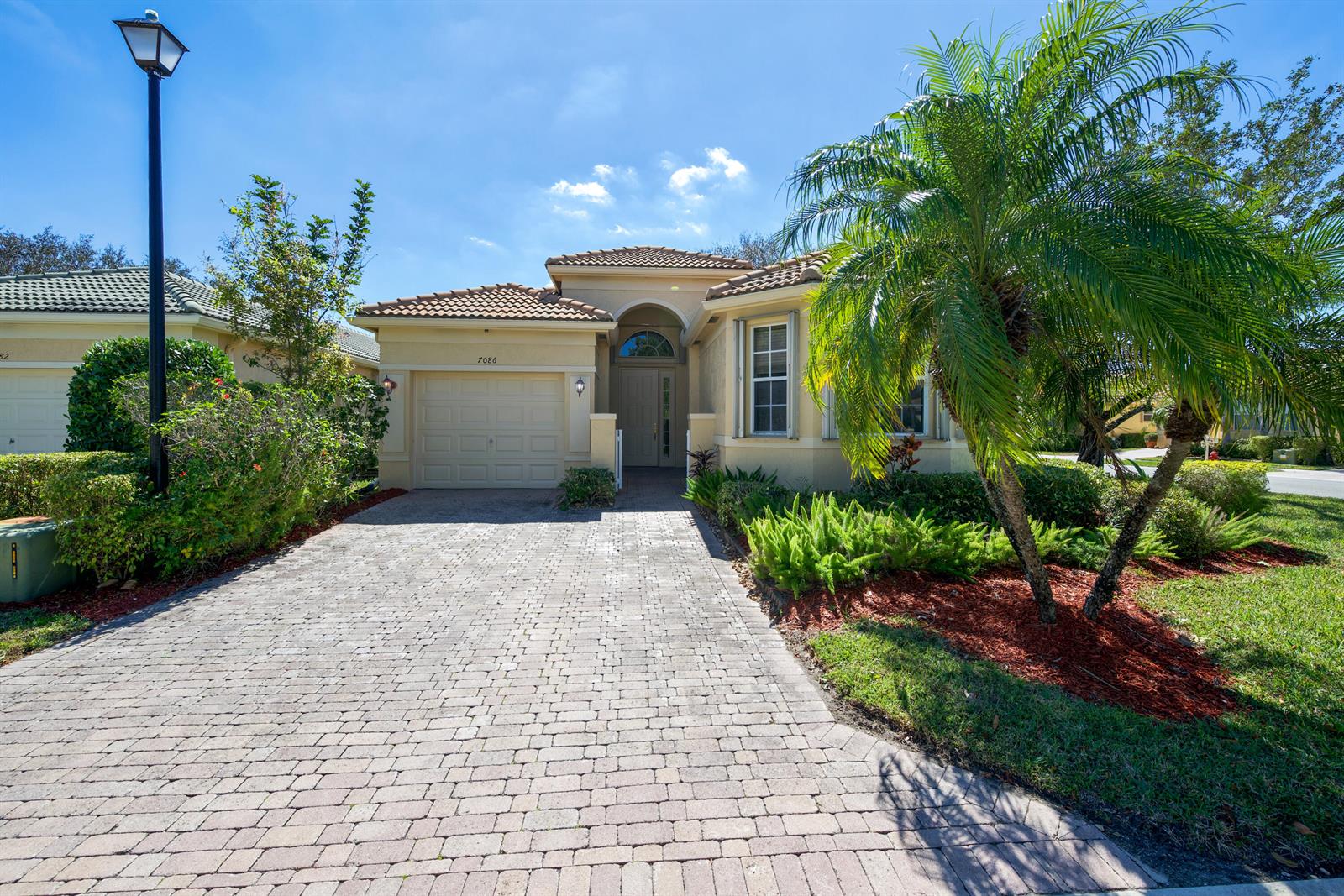 A single-story house with a paved driveway, a garage, and a palm tree in front — 7086 Del Corso Lane, Delray Beach FL 33446, DELRAY BEACH, FL