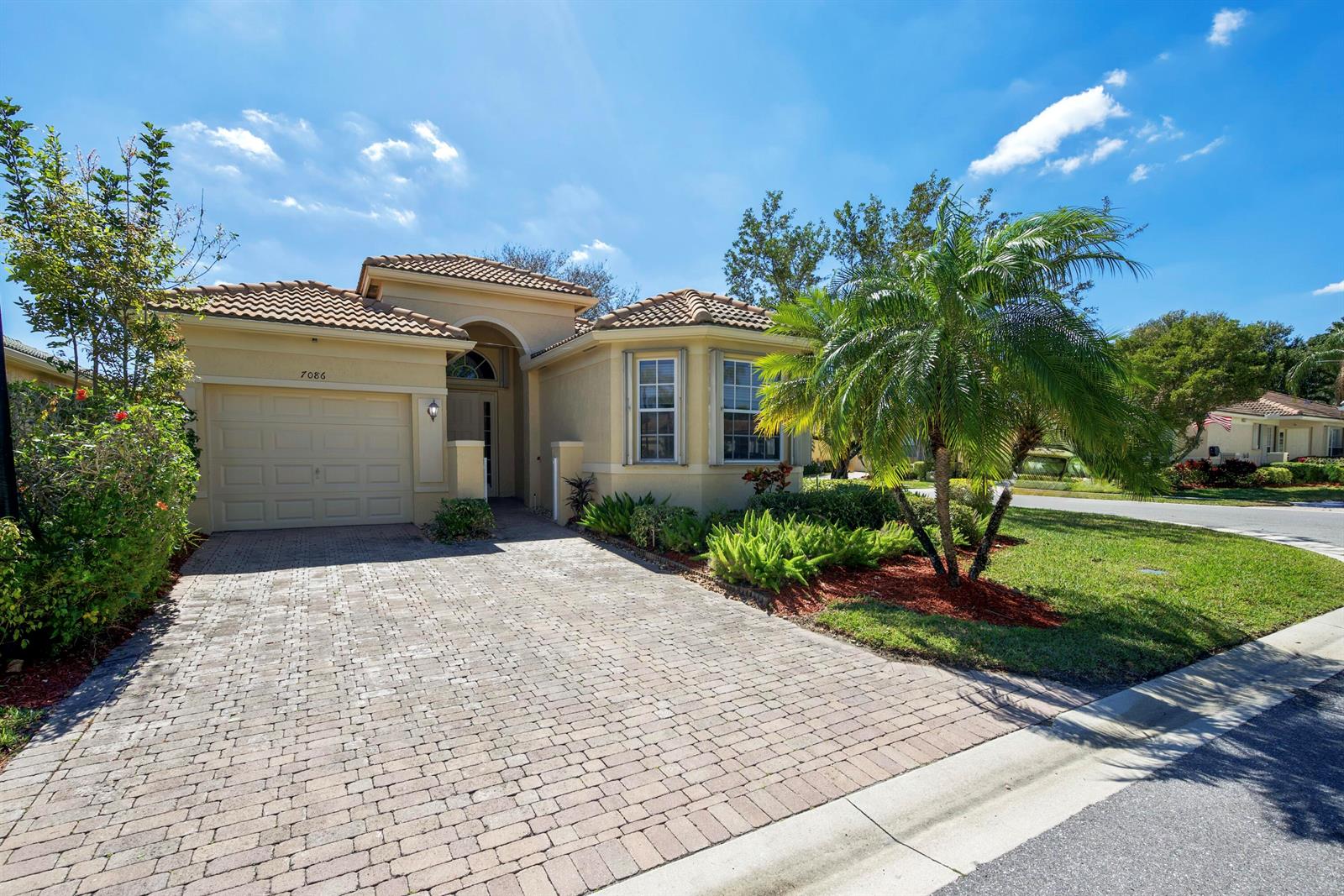 A single-story house with a paved driveway, tan stucco exterior, and a palm tree — 7086 Del Corso Lane, Delray Beach FL 33446, DELRAY BEACH, FL