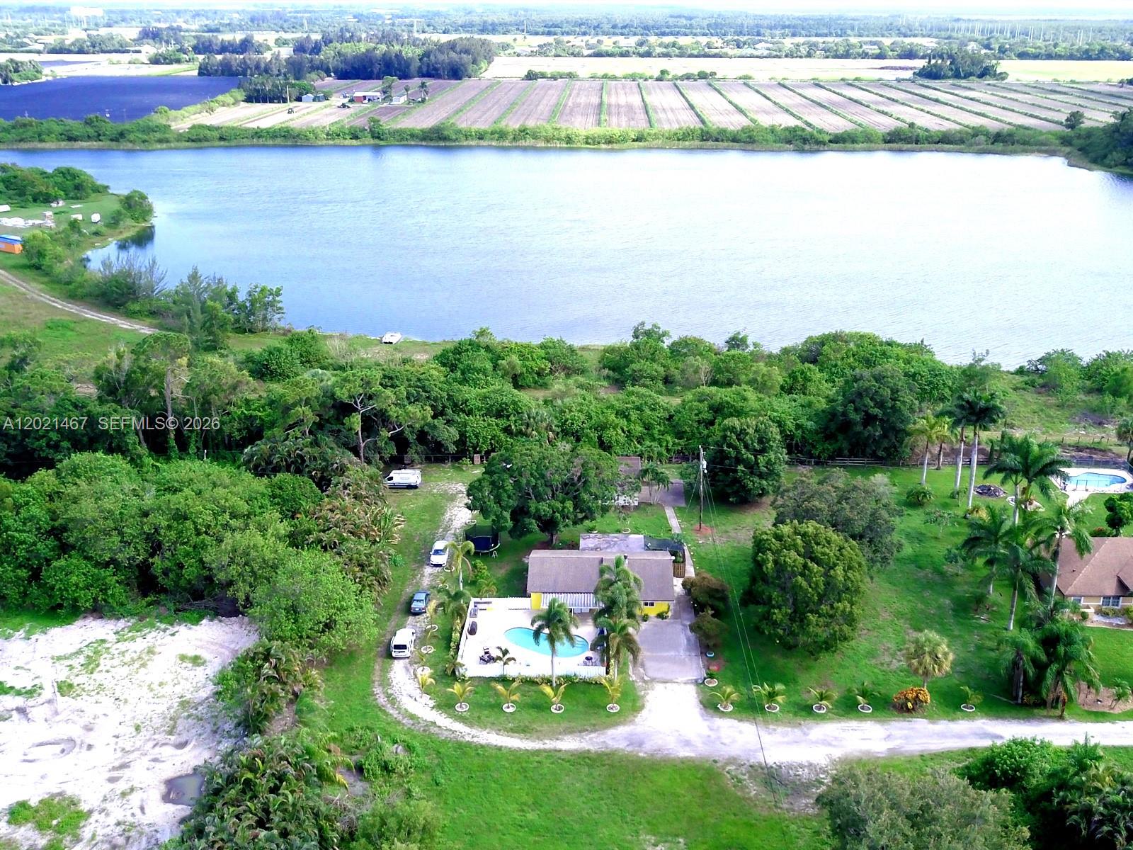 An aerial view shows a house with a pool situated near a large lake — 10646 Barn Rd, Lake Worth FL 33449, LAKE WORTH, FL
