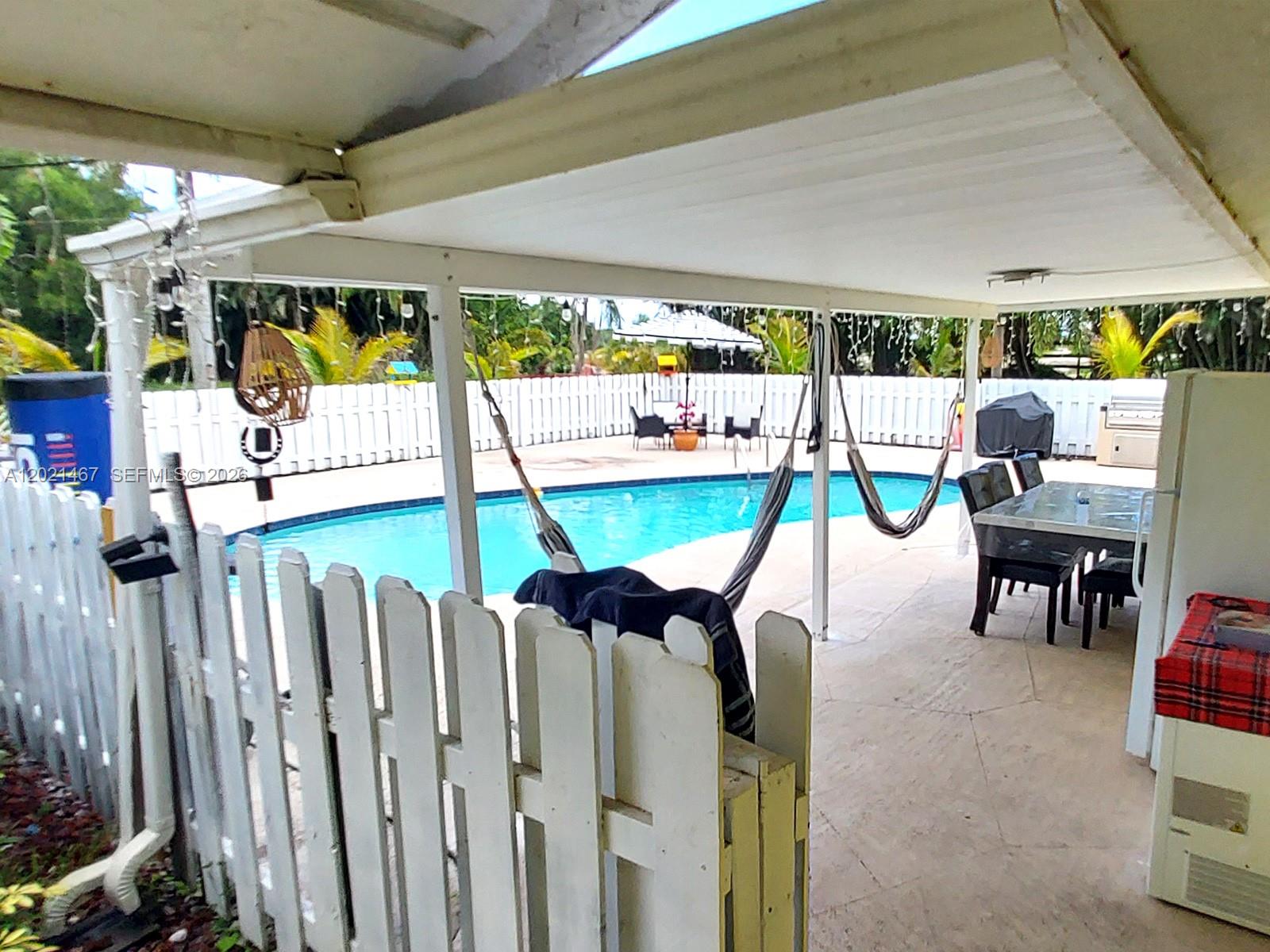 A covered patio overlooks a swimming pool enclosed by a white picket fence — 10646 Barn Rd, Lake Worth FL 33449, LAKE WORTH, FL