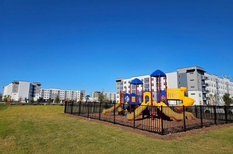 A playground with yellow slides sits inside a fenced area in front of apartment buildings — 5579 MILLENIA BOULEVARD UNIT 110, ORLANDO, FL