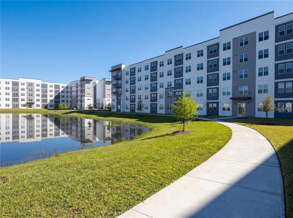 A multi-story apartment building stands next to a retention pond and a concrete walkway — 5579 MILLENIA BOULEVARD UNIT 110, ORLANDO, FL