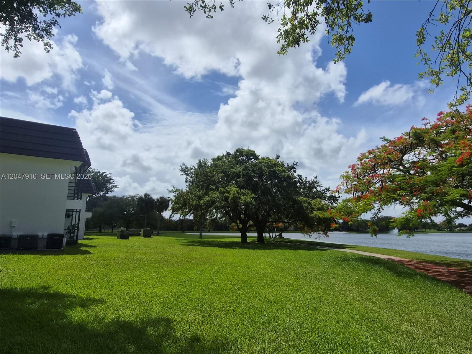 A grassy lawn leads to a large tree and a lake beside a white building — 14913 SW 104th St # 23, Miami FL 33196, MIAMI, FL