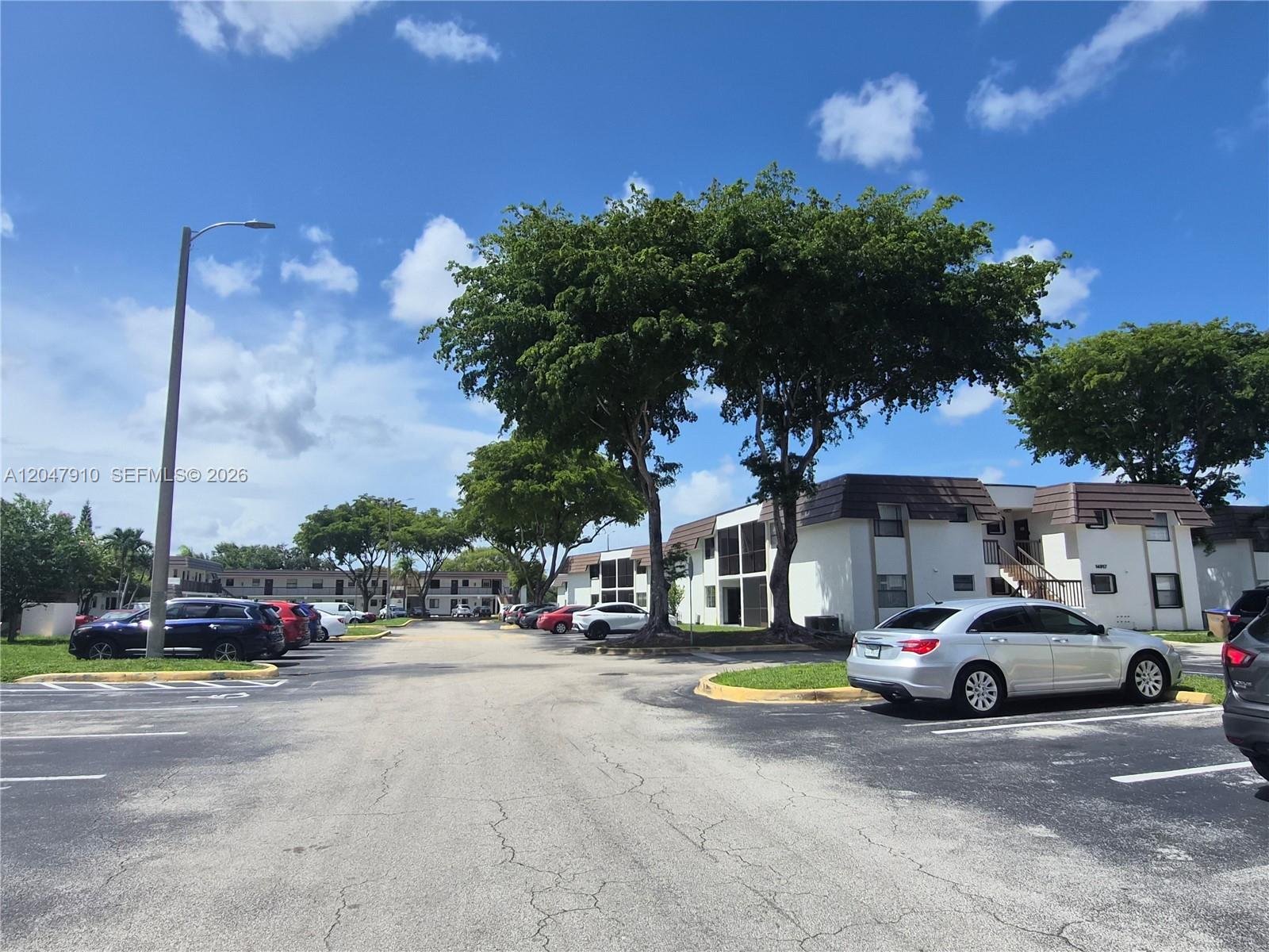 A parking lot sits in front of multi-story apartment buildings under a blue sky — 14913 SW 104th St # 23, Miami FL 33196, MIAMI, FL