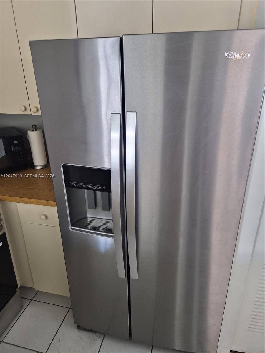 A stainless steel Whirlpool side-by-side refrigerator stands in a kitchen with light-colored cabinets — 14913 SW 104th St # 23, Miami FL 33196, MIAMI, FL