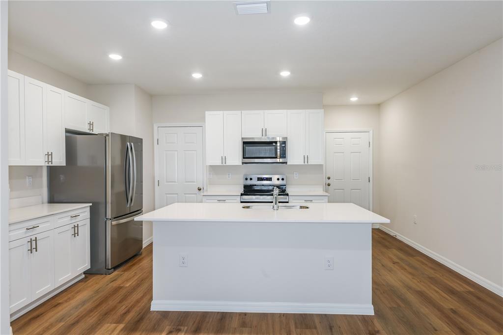 A kitchen features white cabinets, stainless steel appliances, a center island, and wood-look flooring — 9872 PELICAN COAST DRIVE, DADE CITY, FL