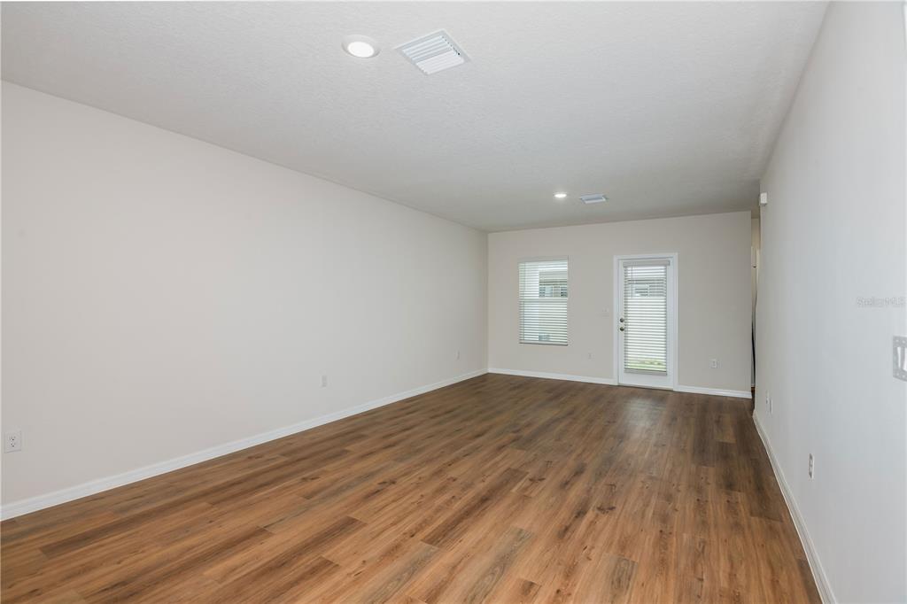 An empty room features light-colored walls, wood-look flooring, a window, and a glass-paneled door — 9872 PELICAN COAST DRIVE, DADE CITY, FL