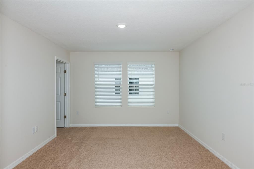An empty bedroom features beige carpet, light-colored walls, two windows with blinds, and a doorway — 9872 PELICAN COAST DRIVE, DADE CITY, FL
