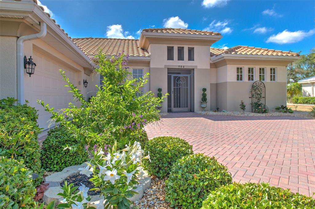 A single-story house with a tiled roof, beige stucco exterior, and a brick paver driveway — 504 RIMINI VISTA WAY, SUN CITY CENTER, FL