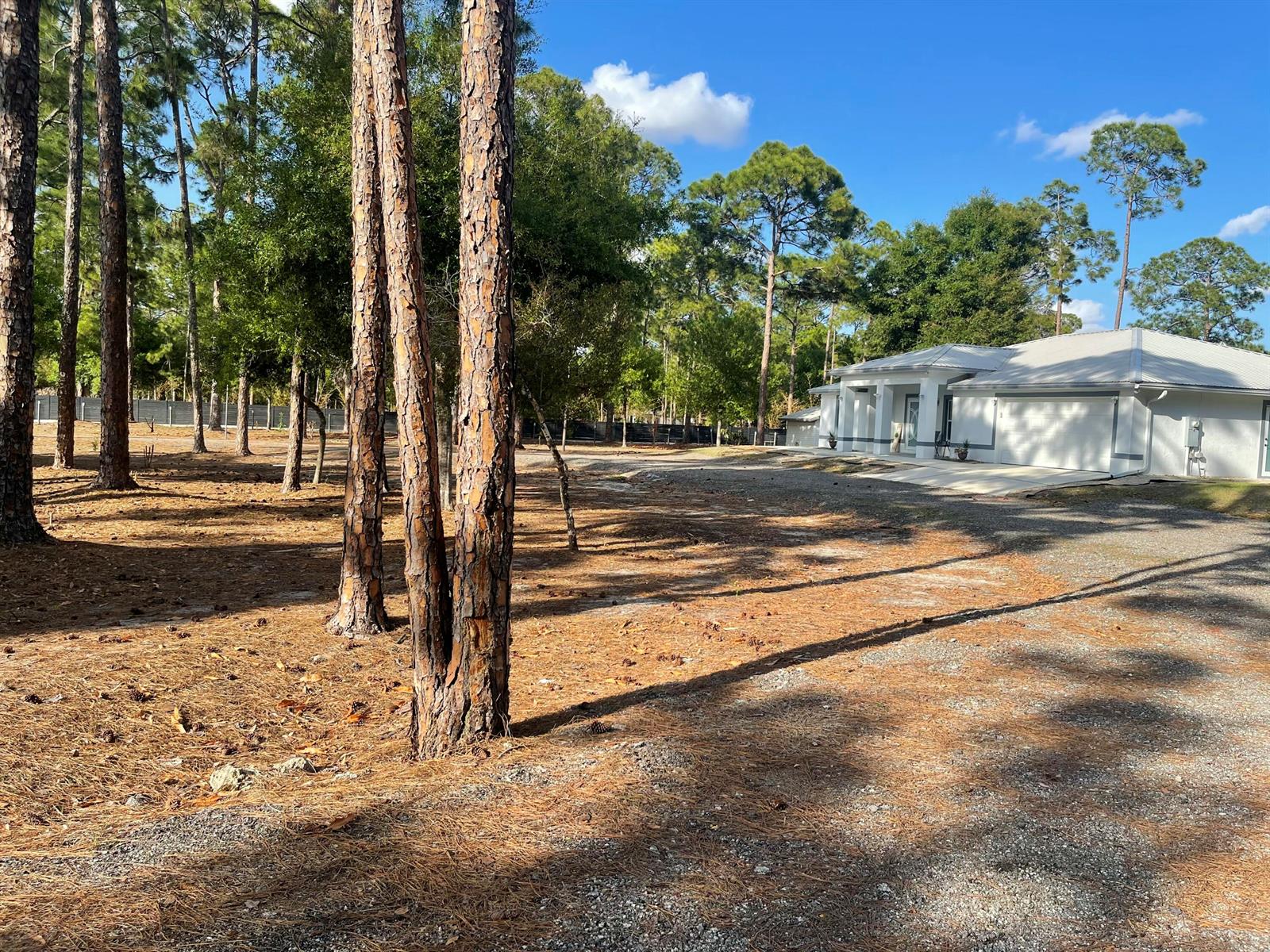 A white house with a garage sits on a gravel lot surrounded by pine trees — 5325 Pioneer 17th Street, Clewiston FL 33440, CLEWISTON, FL