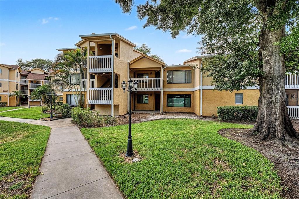 A three-story apartment building with tan stucco walls, white railings, and a paved walkway — 1550 S BELCHER ROAD UNIT 525, CLEARWATER, FL