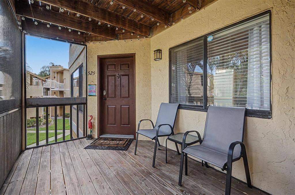 A covered wooden porch features two chairs, a small table, and a brown entry door — 1550 S BELCHER ROAD UNIT 525, CLEARWATER, FL