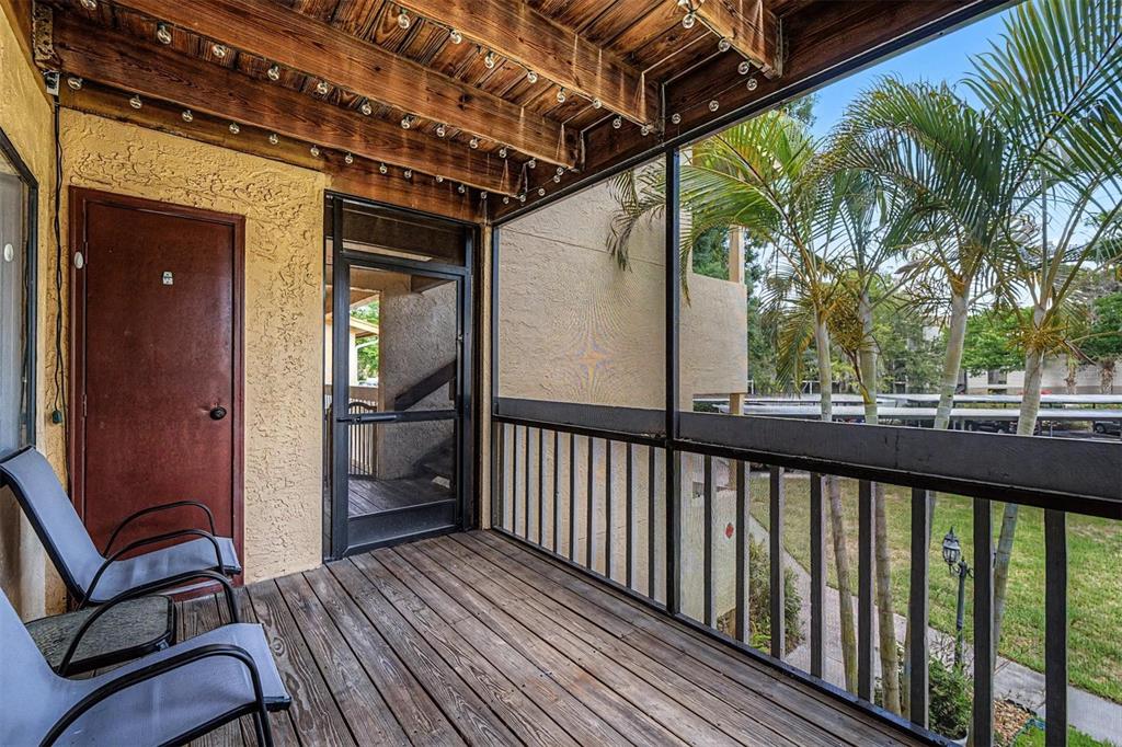 A wooden balcony features a screen enclosure, two chairs, and a view of palm trees — 1550 S BELCHER ROAD UNIT 525, CLEARWATER, FL