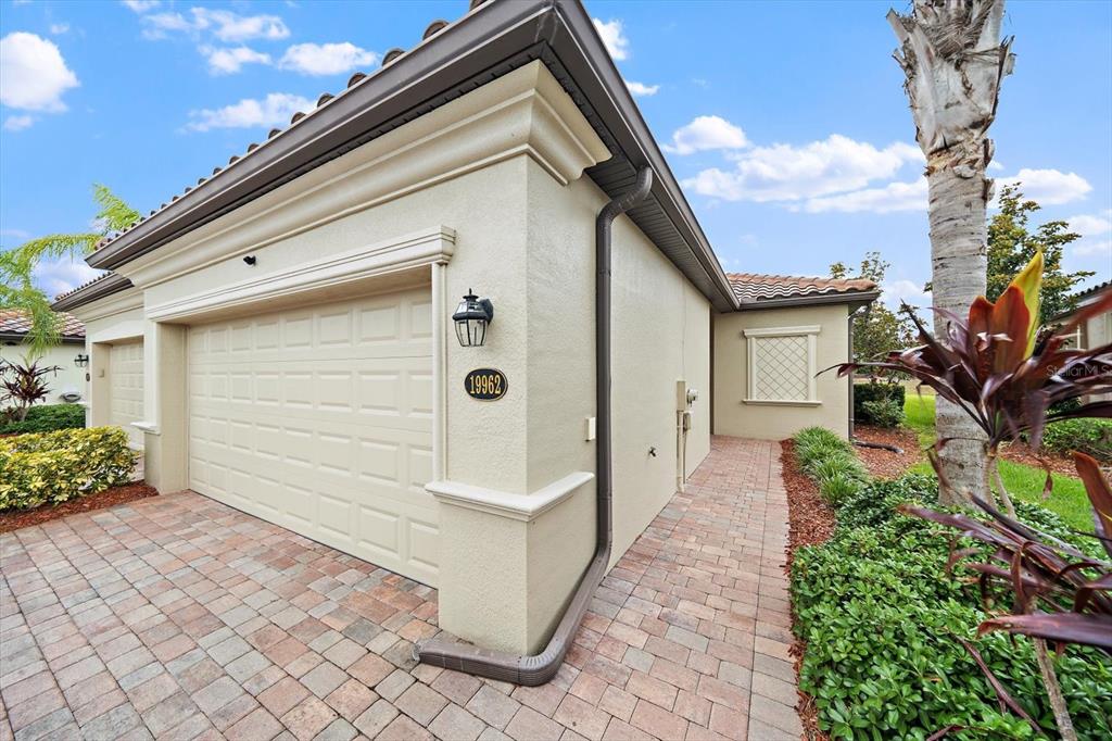 A beige stucco house exterior features a garage, a brick paver driveway, and a walkway — 19962 BENISSIMO DRIVE, VENICE, FL