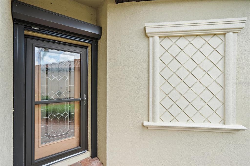 A dark-framed glass door sits next to a decorative wall panel with a lattice design — 19962 BENISSIMO DRIVE, VENICE, FL
