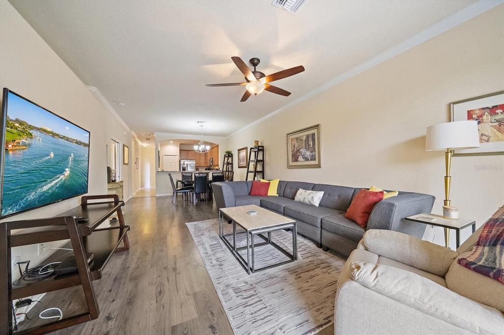 A living room features a grey sectional sofa, wood-look flooring, and an open kitchen — 19962 BENISSIMO DRIVE, VENICE, FL