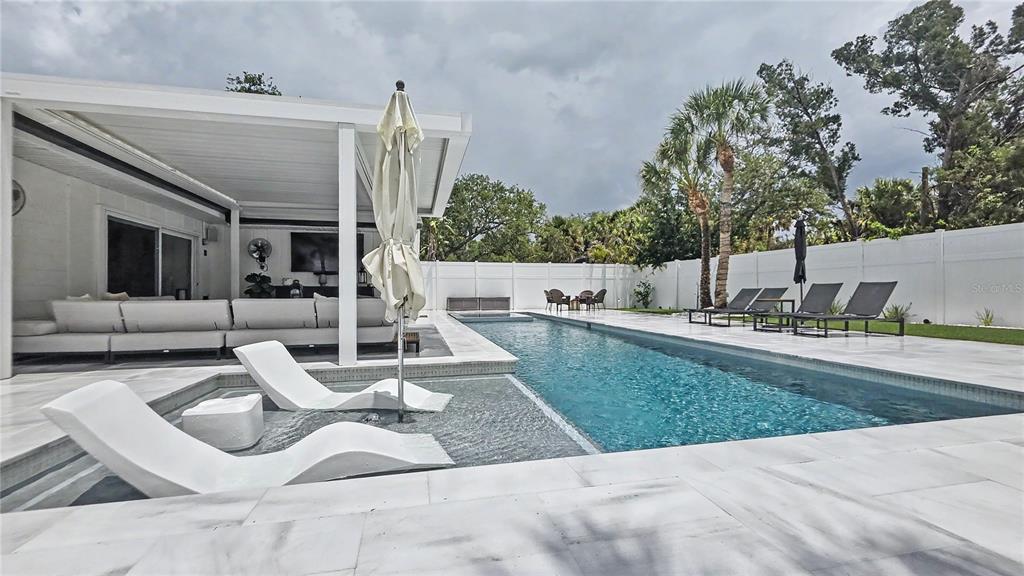A covered patio features a fire pit, seating, a television, and a swimming pool — 5143 SANDY BEACH AVENUE, SARASOTA, FL