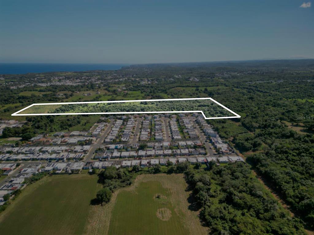 An aerial view shows a large, undeveloped plot of land outlined in white near residential housing — MASIONES DEL ATLANTICO, ISABELA, PR