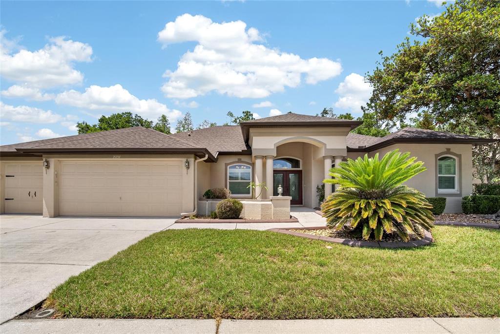 A single-story house with a beige stucco exterior, a three-car garage, and a palm tree — 21234 TANGOR ROAD, LAND O LAKES, FL