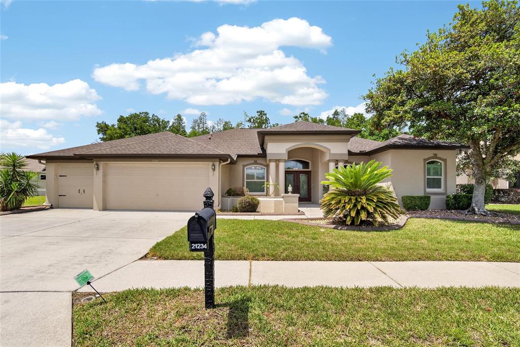 A single-story house with a beige stucco exterior, a three-car garage, and a front lawn — 21234 TANGOR ROAD, LAND O LAKES, FL