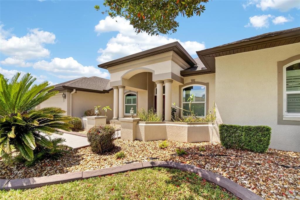 The exterior of a beige stucco house features a covered entryway with columns and landscaping — 21234 TANGOR ROAD, LAND O LAKES, FL