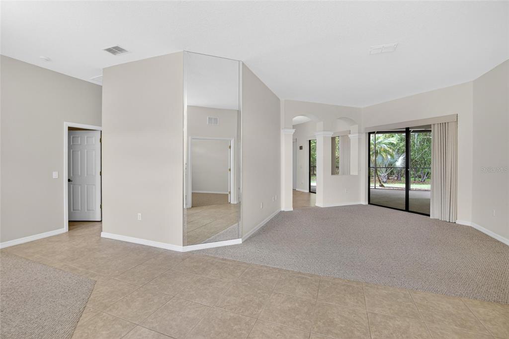 A living room features beige walls, neutral carpeting, tile flooring, and a large corner mirror — 21234 TANGOR ROAD, LAND O LAKES, FL