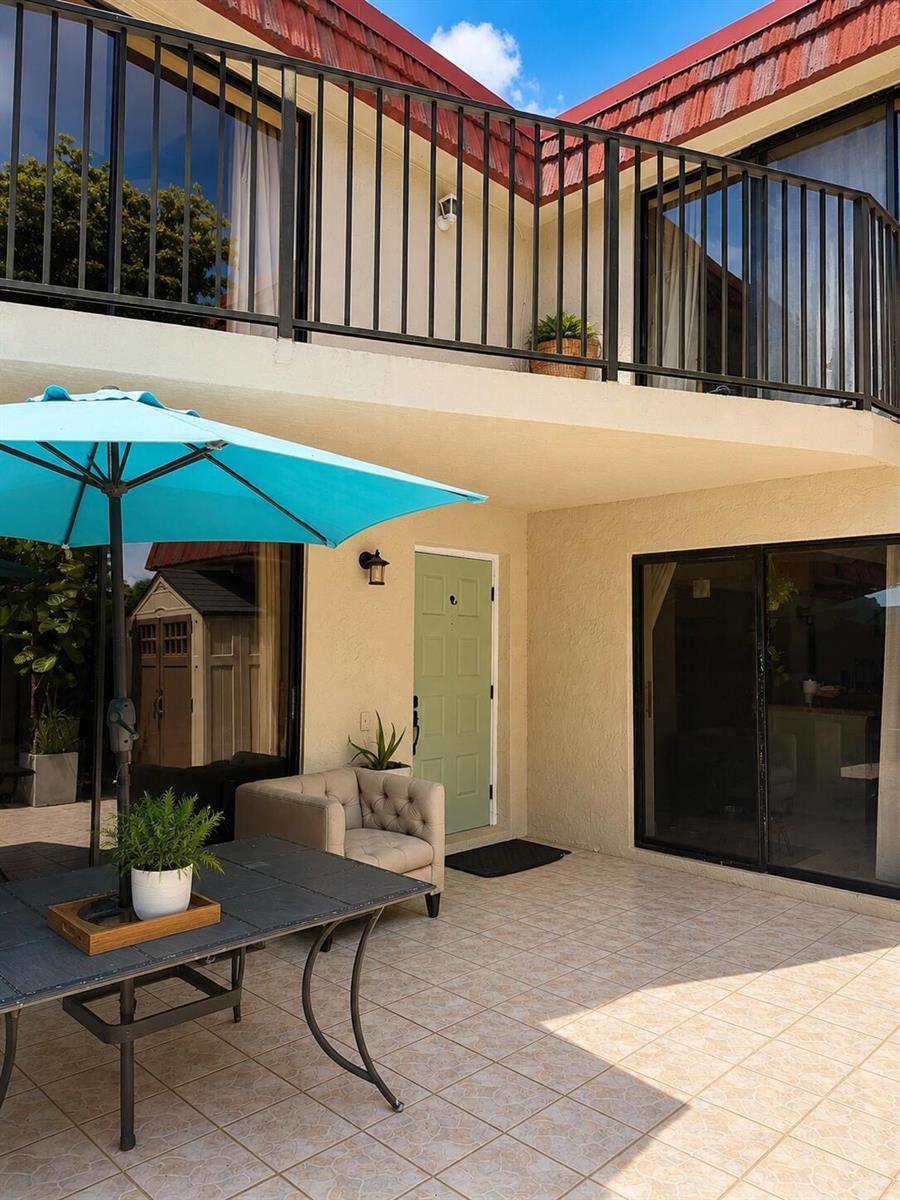A patio features a dining table, a light blue umbrella, and a beige armchair — 8259 Boca Rio, Boca Raton FL 33433, BOCA RATON, FL