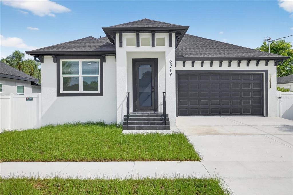 A single-story house features white stucco walls, a dark garage door, and a front entryway — 2719 W SAINT JOHN STREET, TAMPA, FL