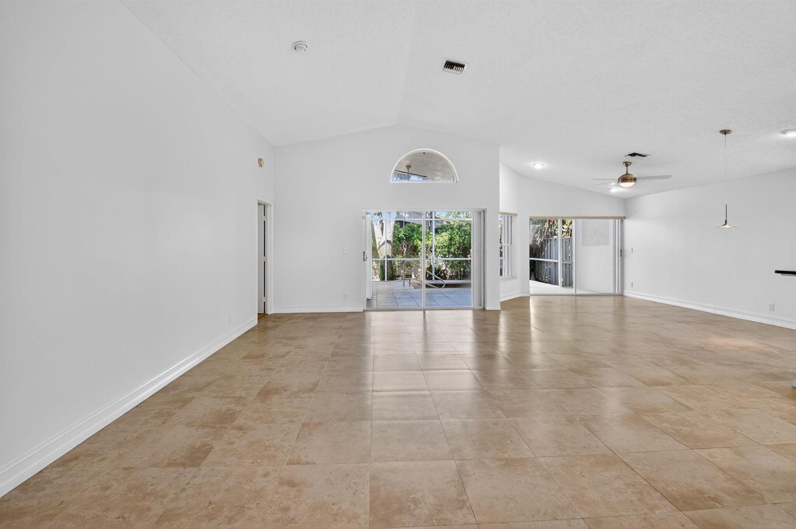 A spacious, empty living room features vaulted ceilings, light-colored tile flooring, and sliding glass doors — 9914 Harbour Lake Circle, Boynton Beach FL 33437, BOYNTON BEACH, FL