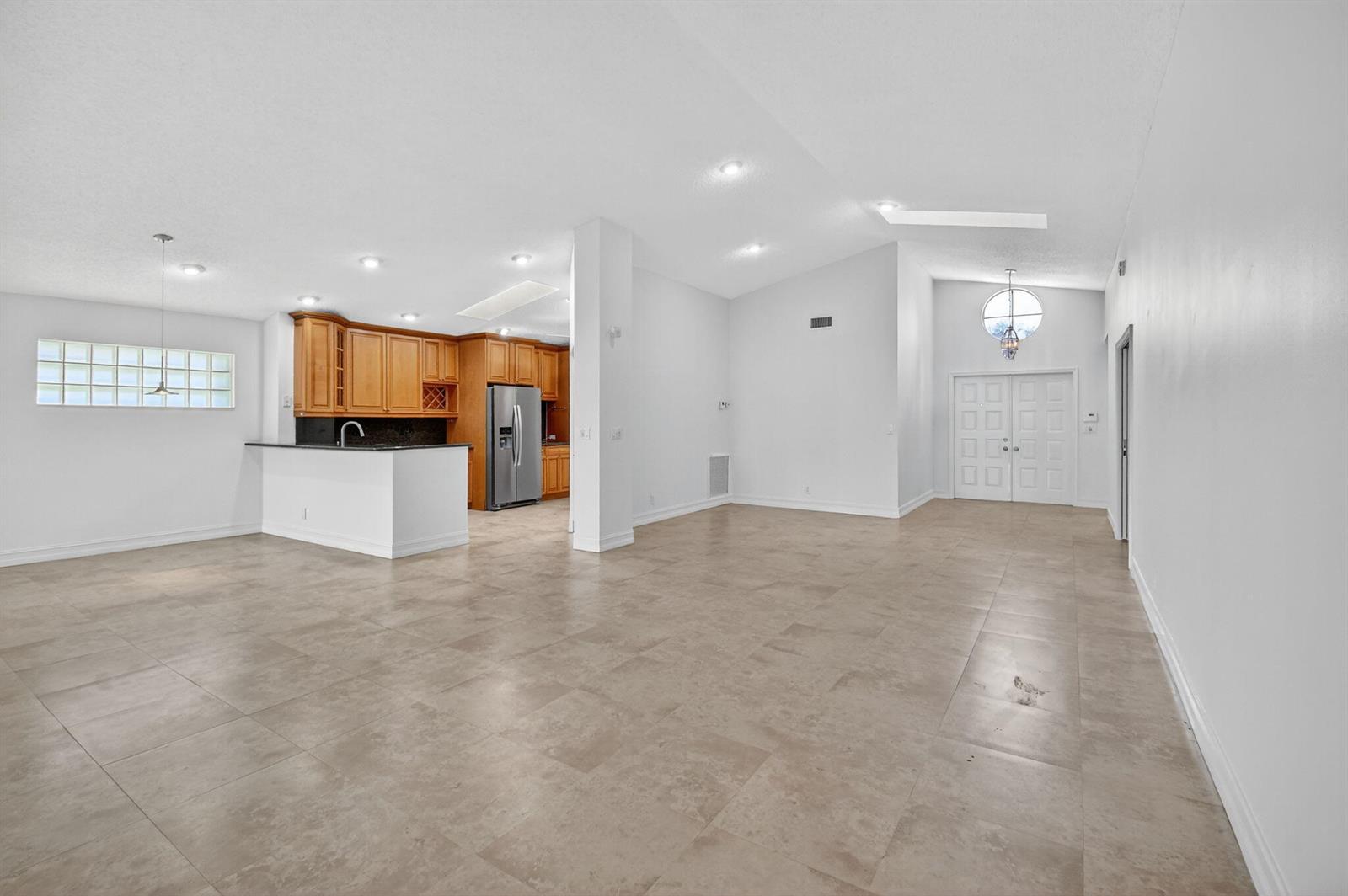 An open-concept living area features light tile flooring, white walls, and a kitchen with wood cabinets — 9914 Harbour Lake Circle, Boynton Beach FL 33437, BOYNTON BEACH, FL