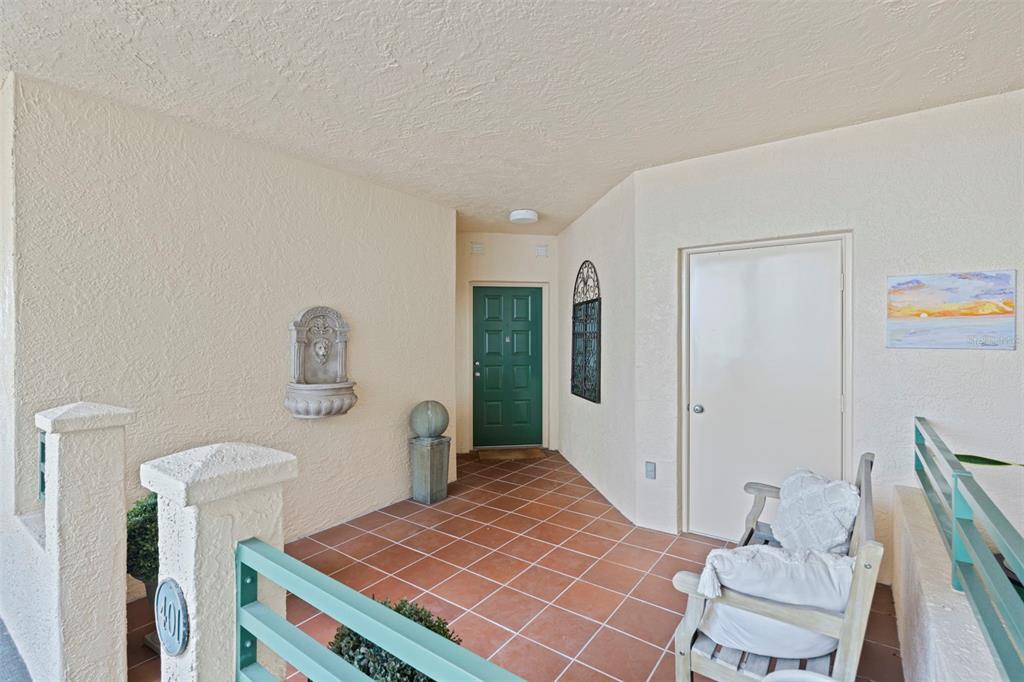 A covered patio features terracotta tile flooring, a green front door, and a wall fountain — 4737 DOLPHIN CAY LANE S UNIT 401, ST PETERSBURG, FL