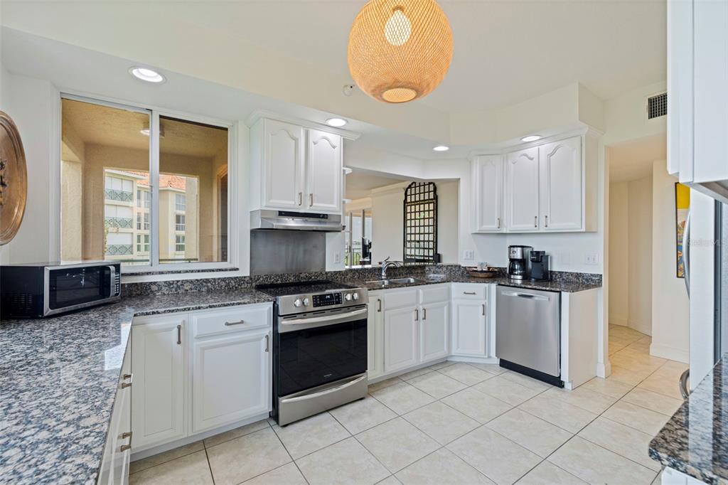 A kitchen with white cabinets, granite countertops, stainless steel appliances, and tile flooring — 4737 DOLPHIN CAY LANE S UNIT 401, ST PETERSBURG, FL