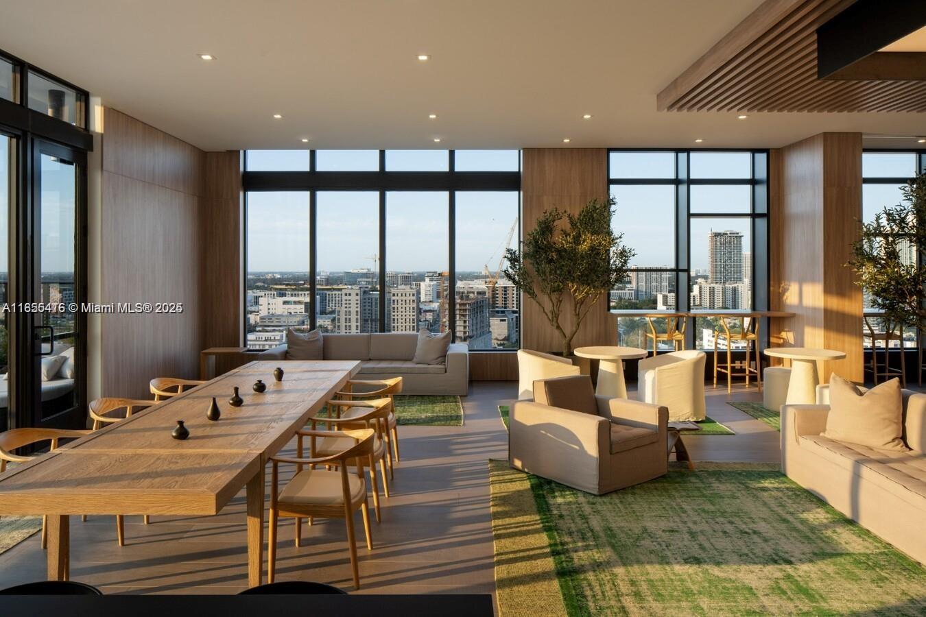 A modern, sunlit lounge features wooden tables, neutral seating, green rugs, and floor-to-ceiling windows — 23 NE 17th Ter, Miami FL 33132, MIAMI, FL