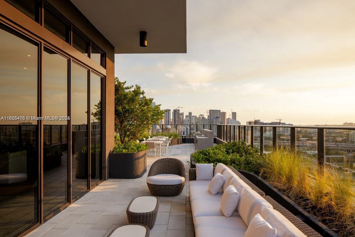 A modern balcony features outdoor lounge furniture, planters, and a view of the city skyline — 23 NE 17th Ter, Miami FL 33132, MIAMI, FL