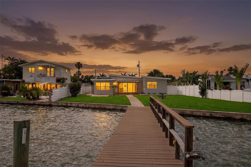 A wooden dock extends into a waterway with a white boat moored alongside — 708 SUNSET COVE, MADEIRA BEACH, FL