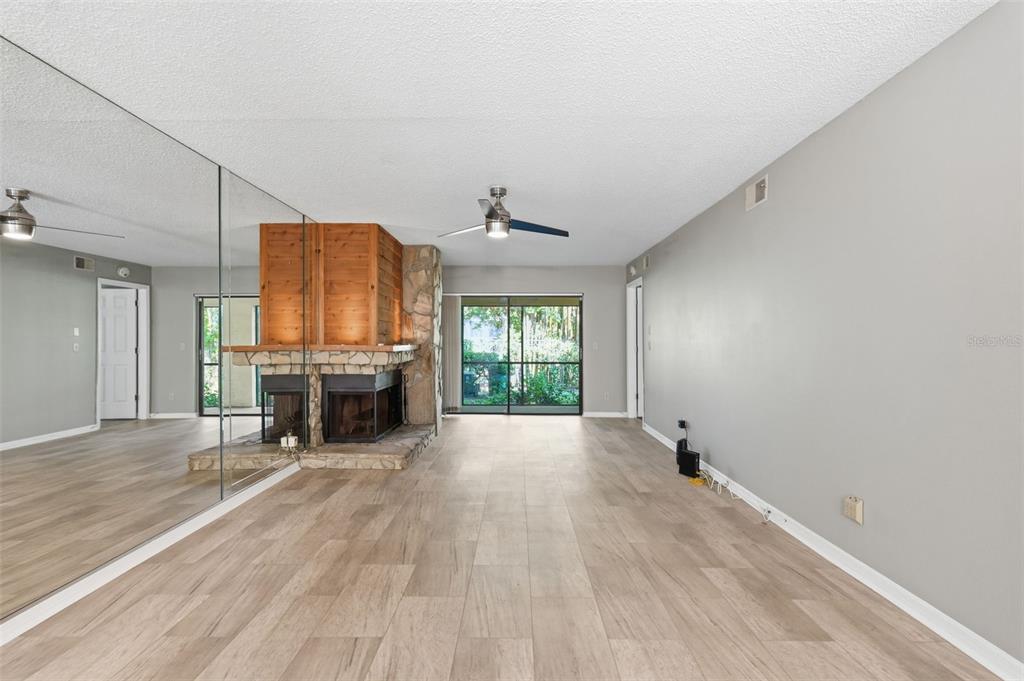 A living room features light wood-look flooring, a stone fireplace, and a mirrored wall — 3163 LANDMARK DRIVE UNIT 615, CLEARWATER, FL