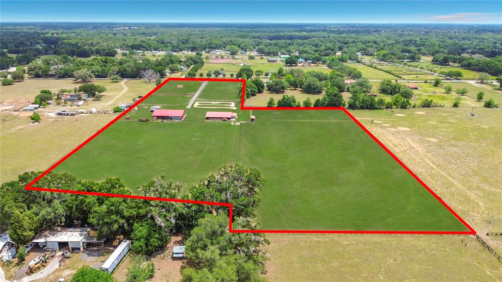 An aerial view shows a large, fenced pasture with two red-roofed barns and trees — 16750 SE 19TH COURT, SUMMERFIELD, FL