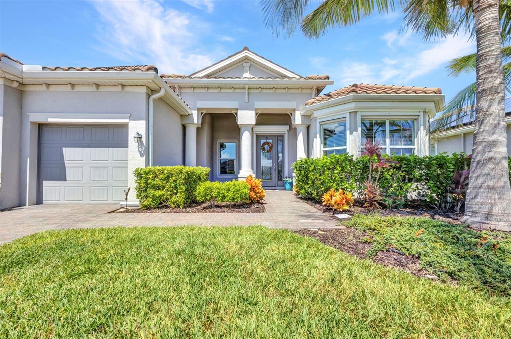 A single-story house exterior features a garage, a covered entryway with columns, and landscaped gardens — 15000 SPANISH POINT DRIVE, PORT CHARLOTTE, FL