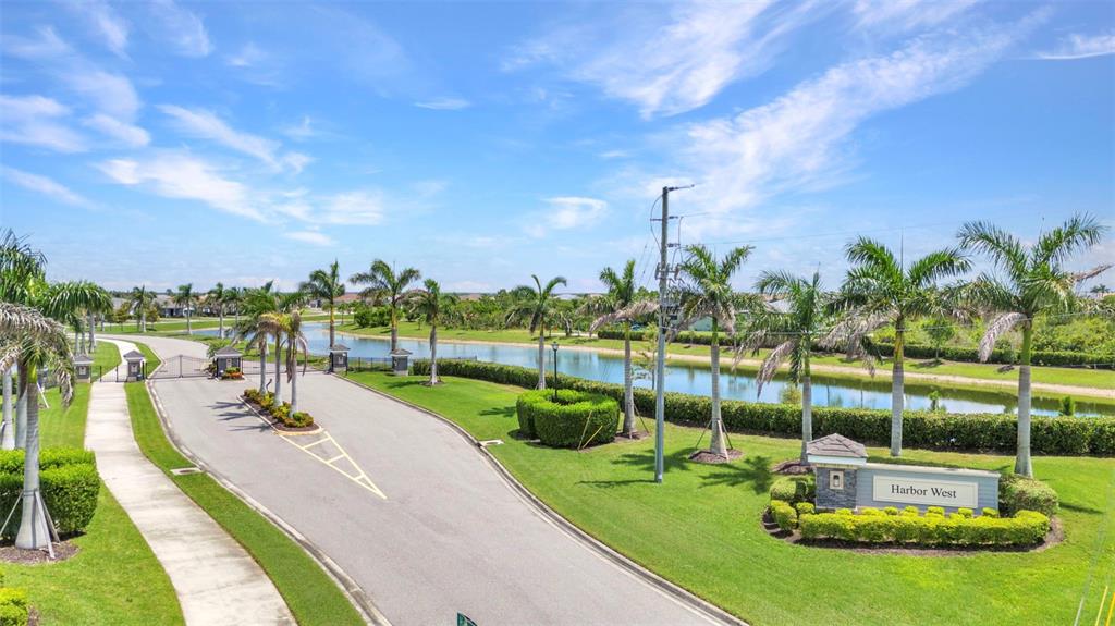 An exterior view of the Harbor West gated community entrance with palm trees and a pond — 15000 SPANISH POINT DRIVE, PORT CHARLOTTE, FL
