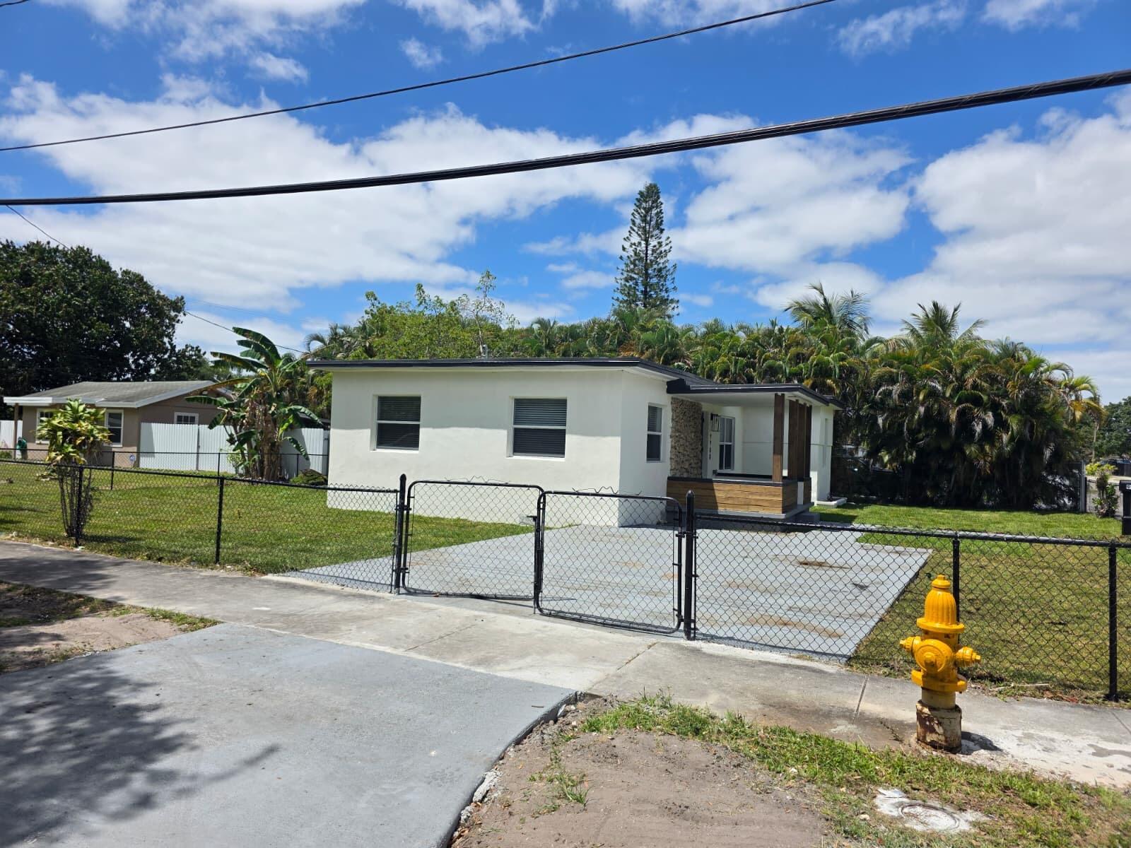 A single-story white house with a concrete driveway and chain-link fence under a blue sky — 9900 NW 25th Avenue, Miami FL 33147, MIAMI, FL