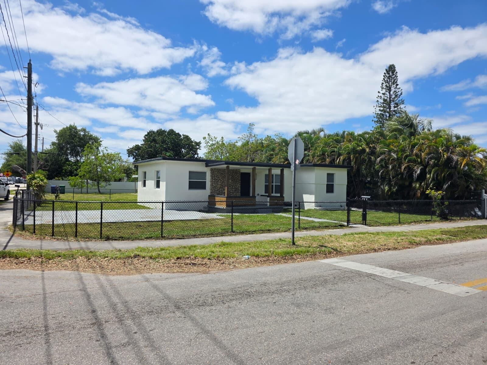 A single-story white house with a stone-accented porch sits behind a black chain-link fence — 9900 NW 25th Avenue, Miami FL 33147, MIAMI, FL