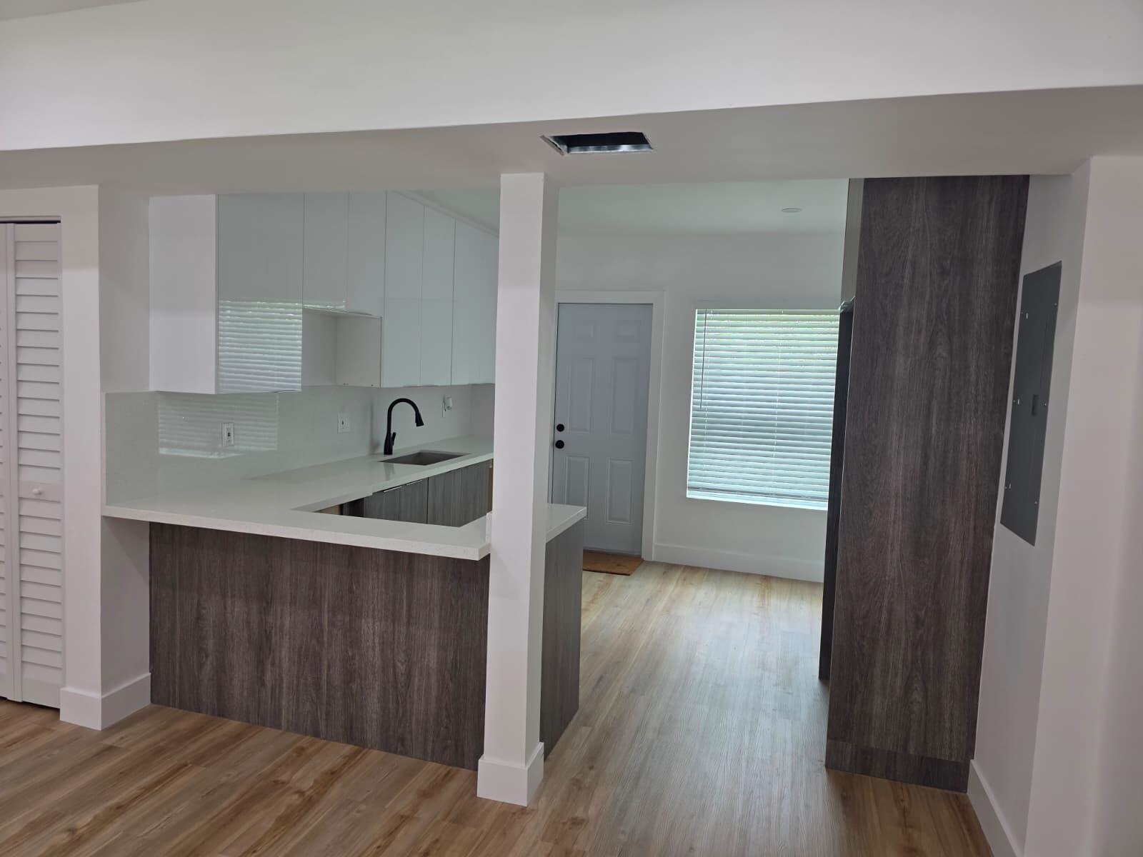 A kitchen features white upper cabinets, dark wood-grain lower cabinets, and light wood flooring — 9900 NW 25th Avenue, Miami FL 33147, MIAMI, FL