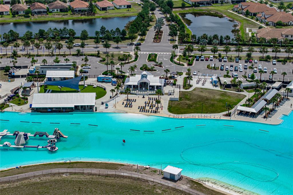 An aerial view shows a large turquoise lagoon with floating inflatables and surrounding recreational facilities — 16833 TRITE BEND STREET, WIMAUMA, FL