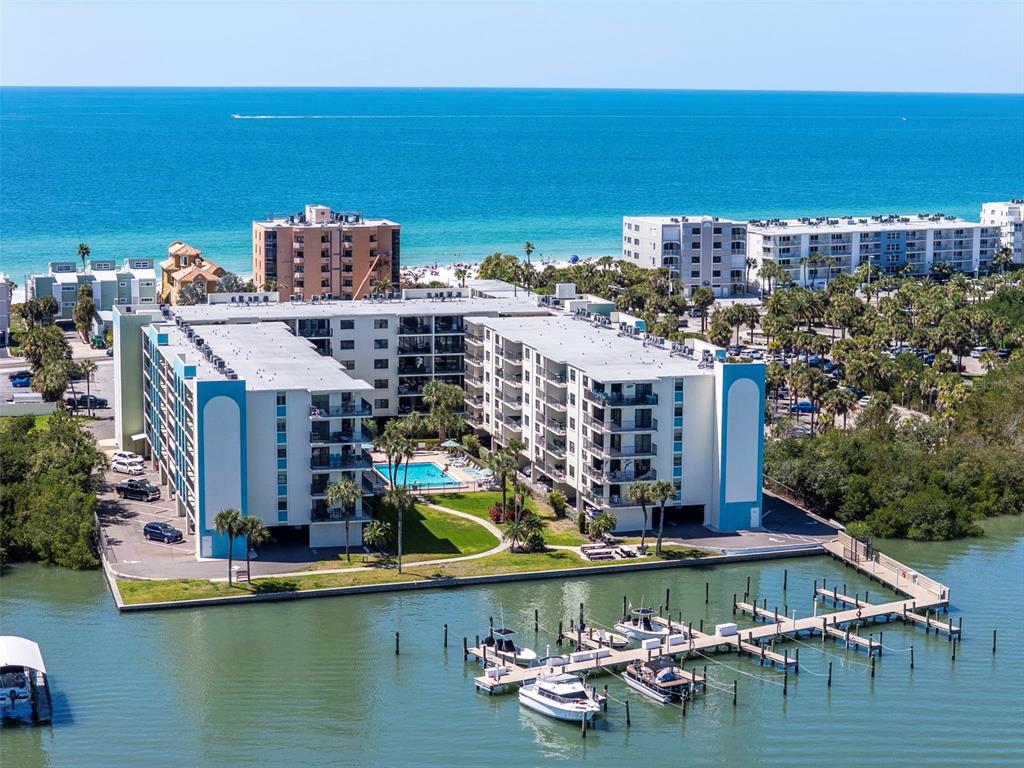 An aerial view shows a multi-story waterfront apartment complex with a pool and boat docks — 19531 GULF BOULEVARD UNIT 414, INDIAN SHORES, FL