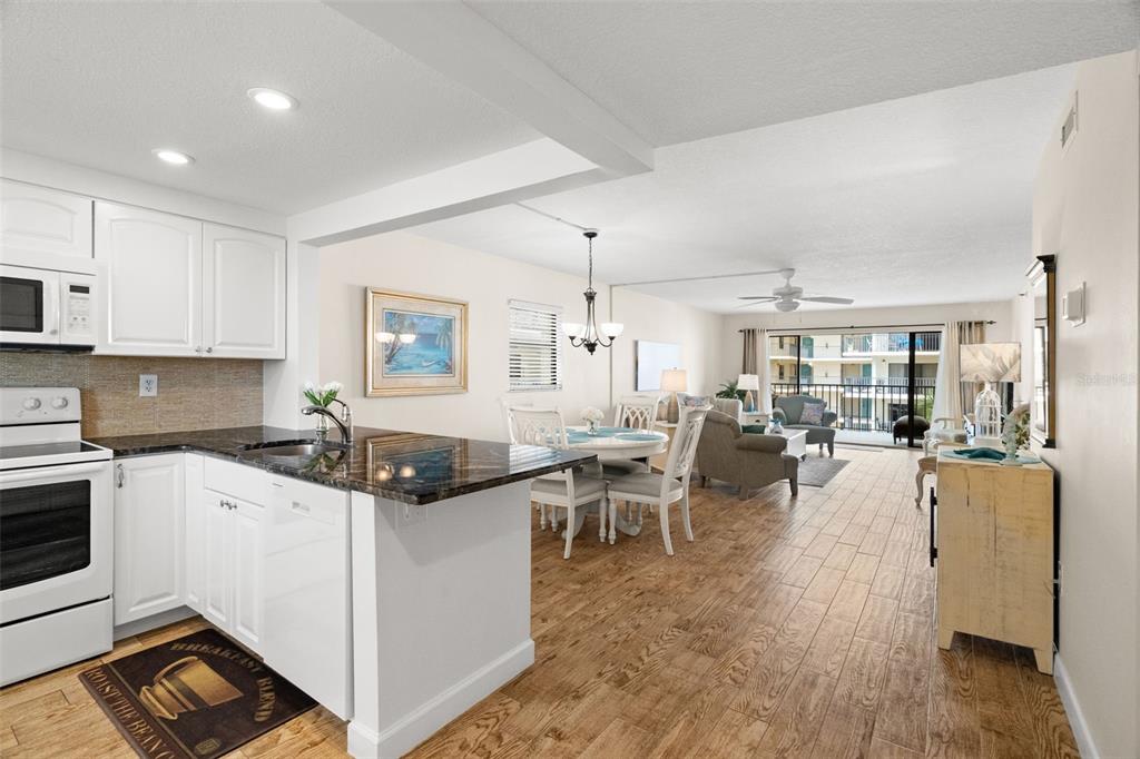 An open-concept kitchen and dining area with wood-look tile flooring and a balcony view — 19531 GULF BOULEVARD UNIT 414, INDIAN SHORES, FL