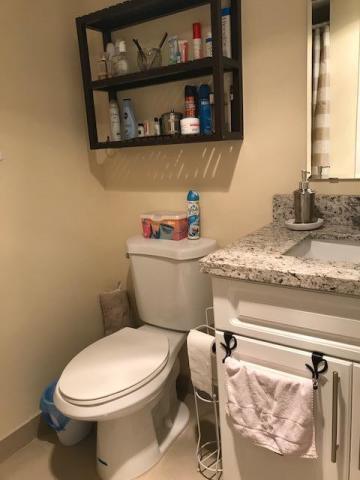 A bathroom features a toilet, a granite-topped vanity, and a wall-mounted wooden storage shelf — 3300 Springdale Boulevard # 301, Palm Springs FL 33461, PALM SPRINGS, FL