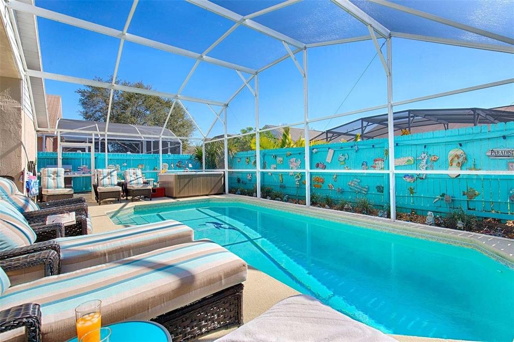 A screened-in swimming pool area with lounge chairs, a hot tub, and a blue fence — 2672 AUTUMN CREEK CIRCLE, KISSIMMEE, FL