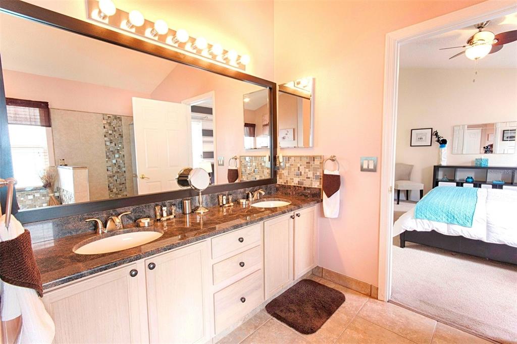 A bathroom with a double vanity, granite countertops, and a large mirror, adjacent to a bedroom — 2672 AUTUMN CREEK CIRCLE, KISSIMMEE, FL